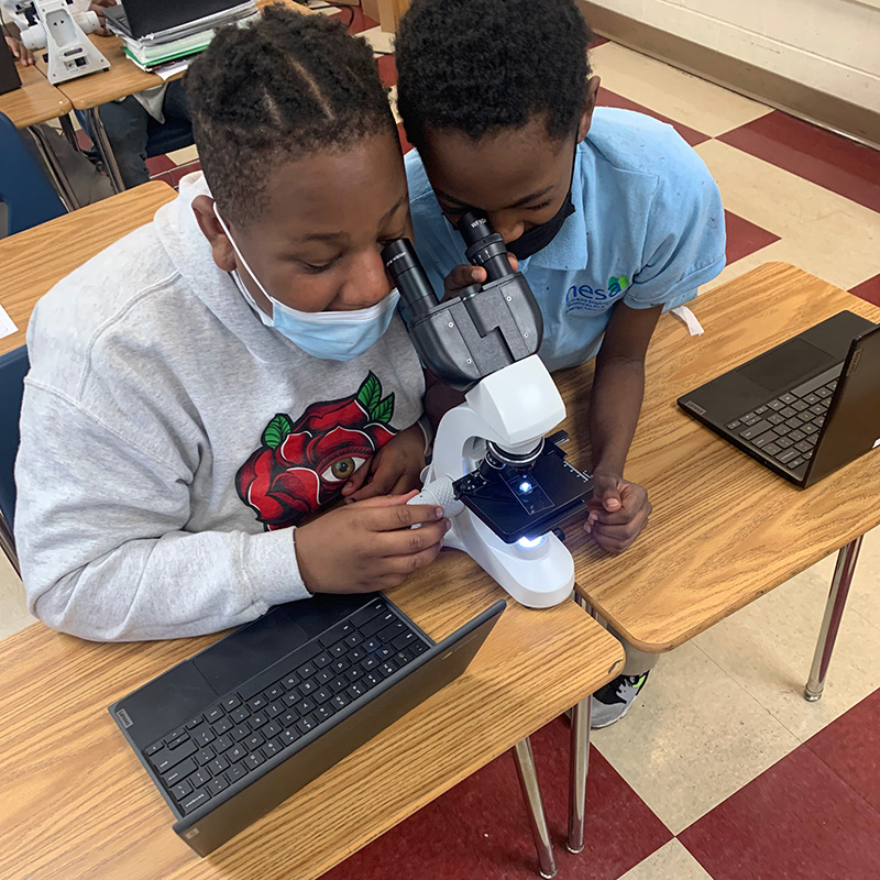 two middle school students looking through a microscope